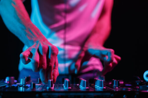 Hands of disc jockey playing electronic music set on stage in night club. Professional audio equipment on techno party
